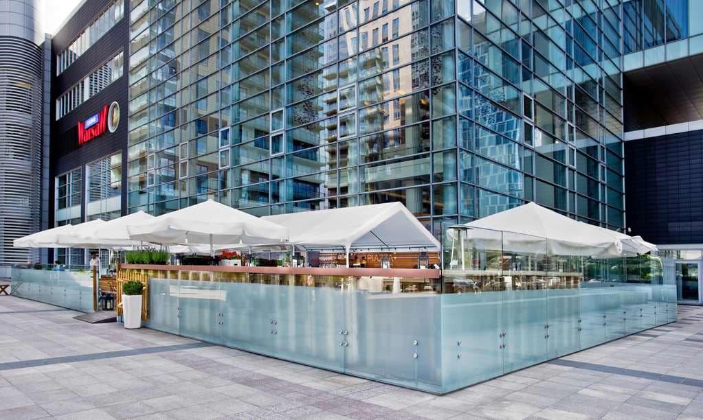 A sleek, modern indoor pool area at Hilton Warsaw City featuring a 25-meter swimming lane, floor-to-ceiling glass windows with city views, and lounge chairs.