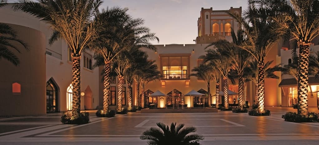 Golden sandstone cliffs of the Al Hajar mountains framing the turquoise waters of the Gulf of Oman at the Barr Al Jissah resort.