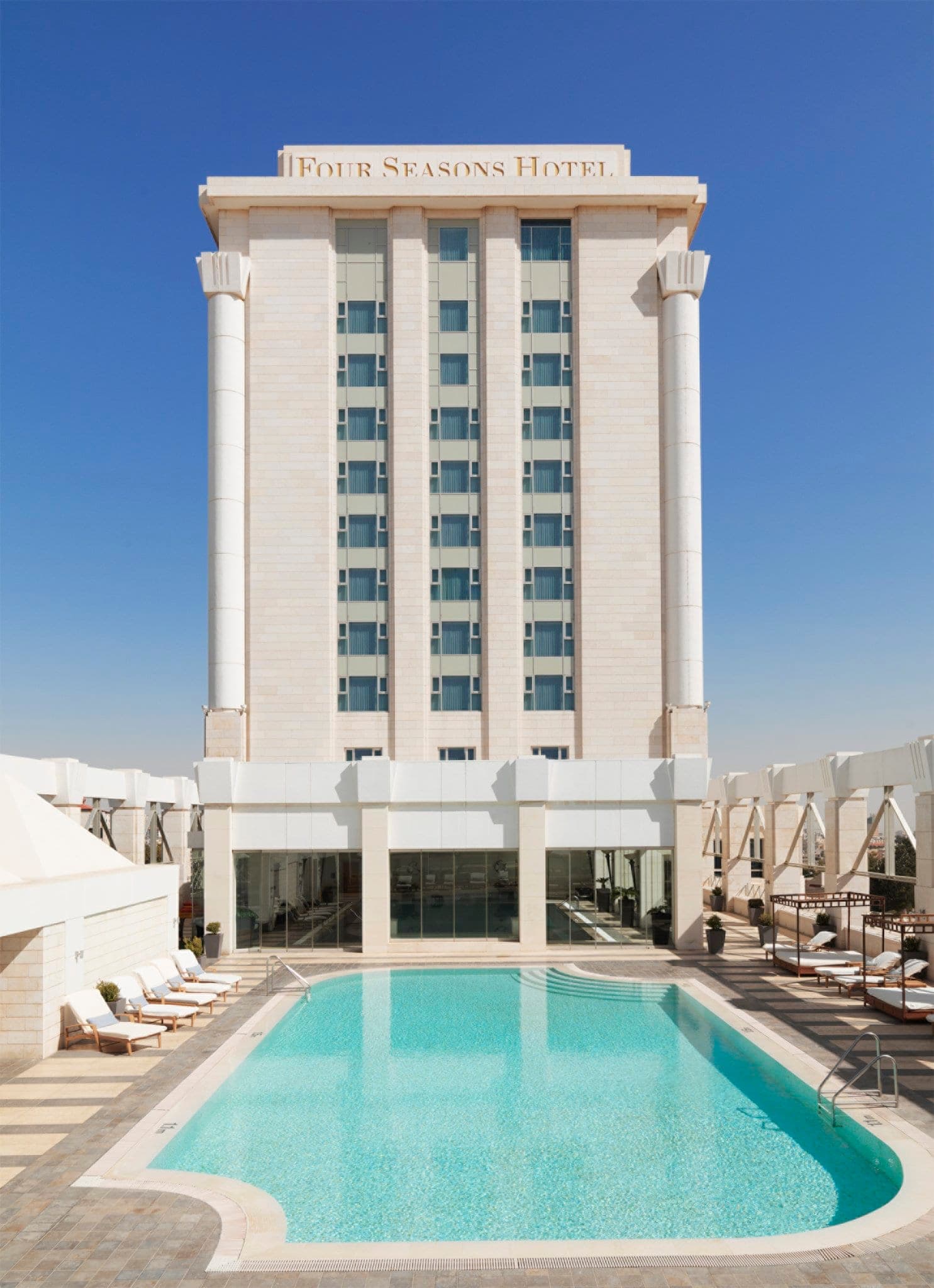 The Romanesque indoor pool at Four Seasons Amman featuring arched windows and mosaic tiling.