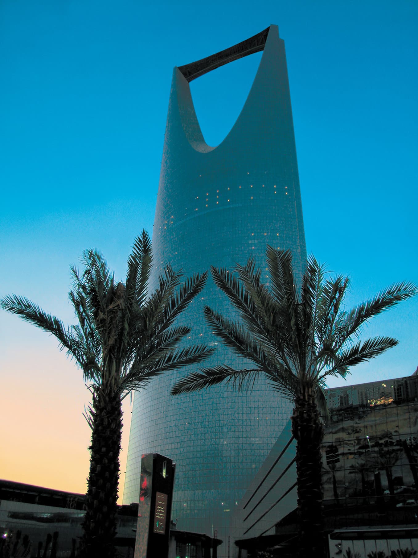 View from a Four Seasons Riyadh suite looking out through floor-to-ceiling windows at the illuminated Riyadh skyline at dusk.