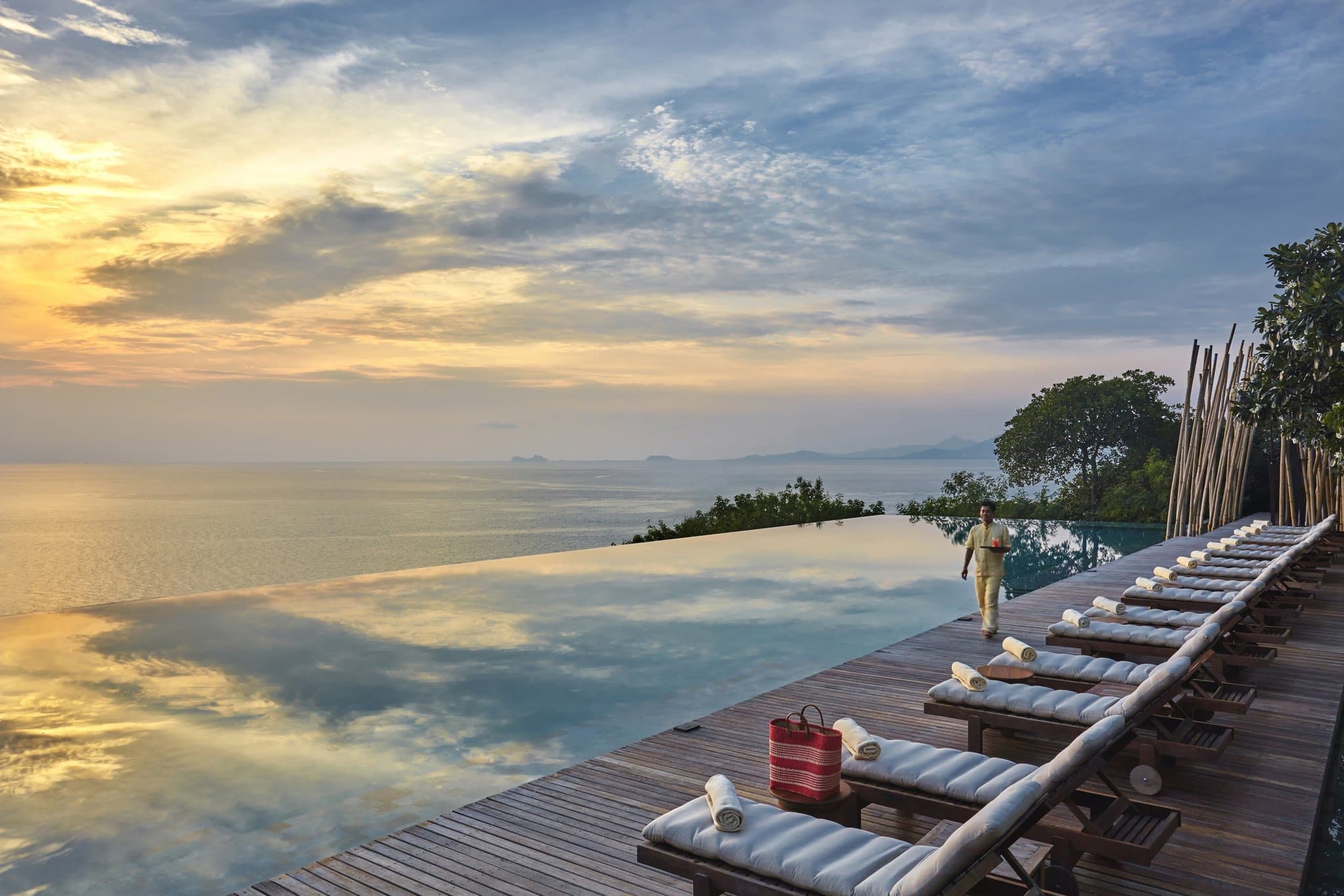 The weathered teak terraces of Dining on the Rocks at Six Senses Samui cantilevered over the ocean at sunset.