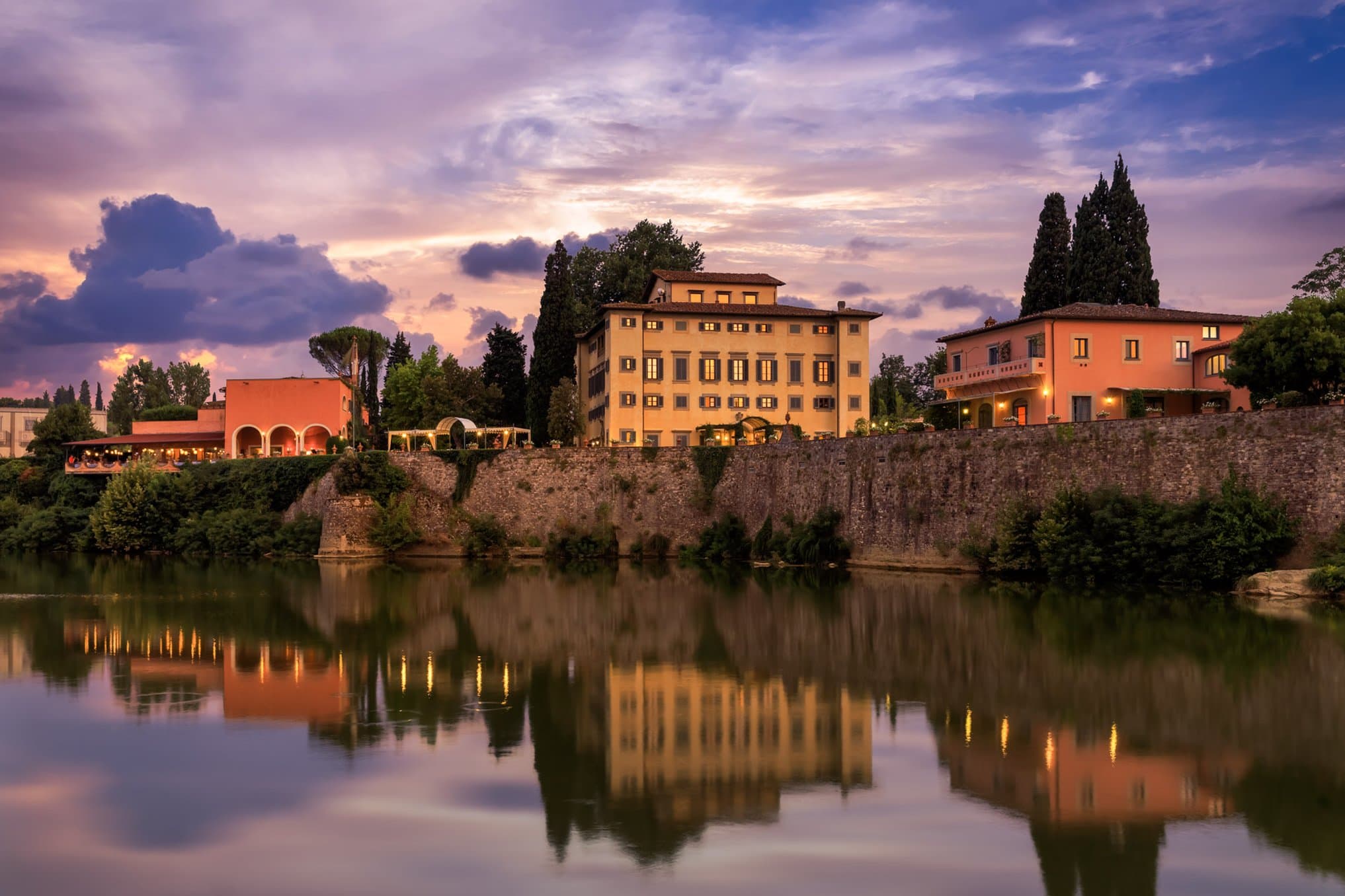 Diners on the terrace of Il Verrocchio restaurant at Villa La Massa overlooking the Arno River at sunset.