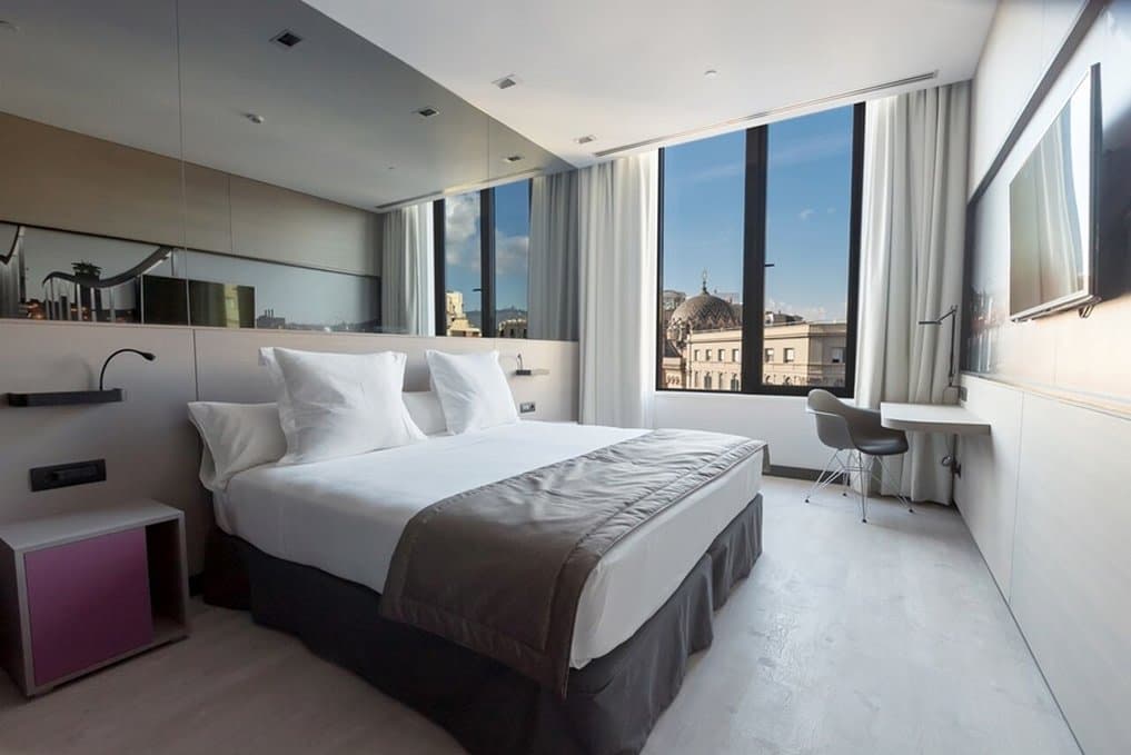 A high-angle shot of the Hotel Negresco Princess rooftop infinity pool with the spires of the Sagrada Família visible in the distance during sunset.