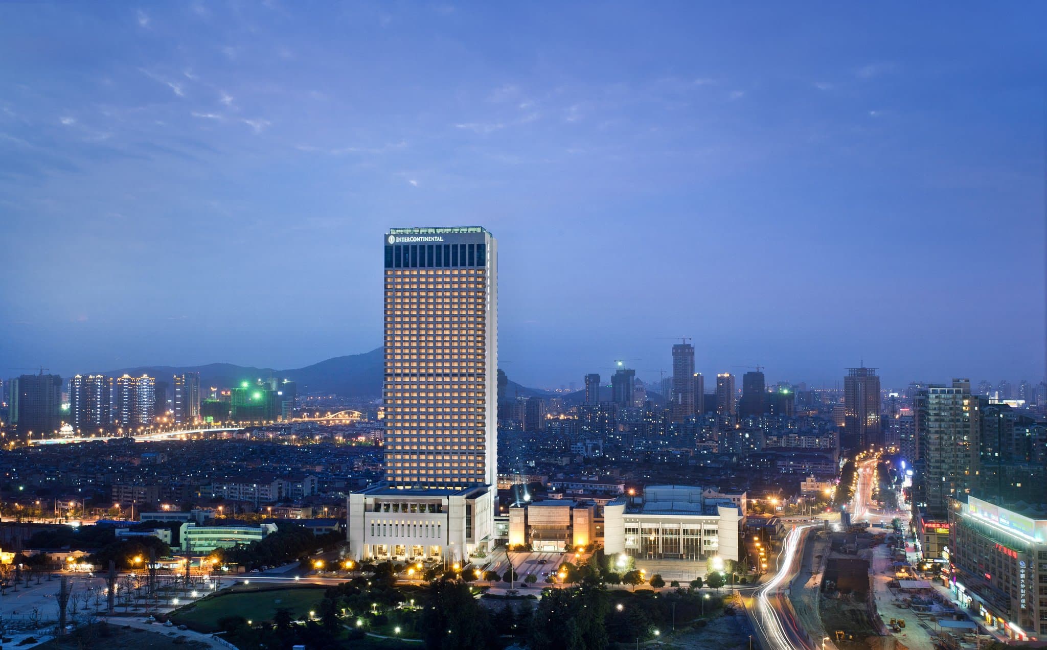 A dramatic silhouette of the InterContinental Wuxi indoor pool against the city night skyline, with floor-to-ceiling windows.