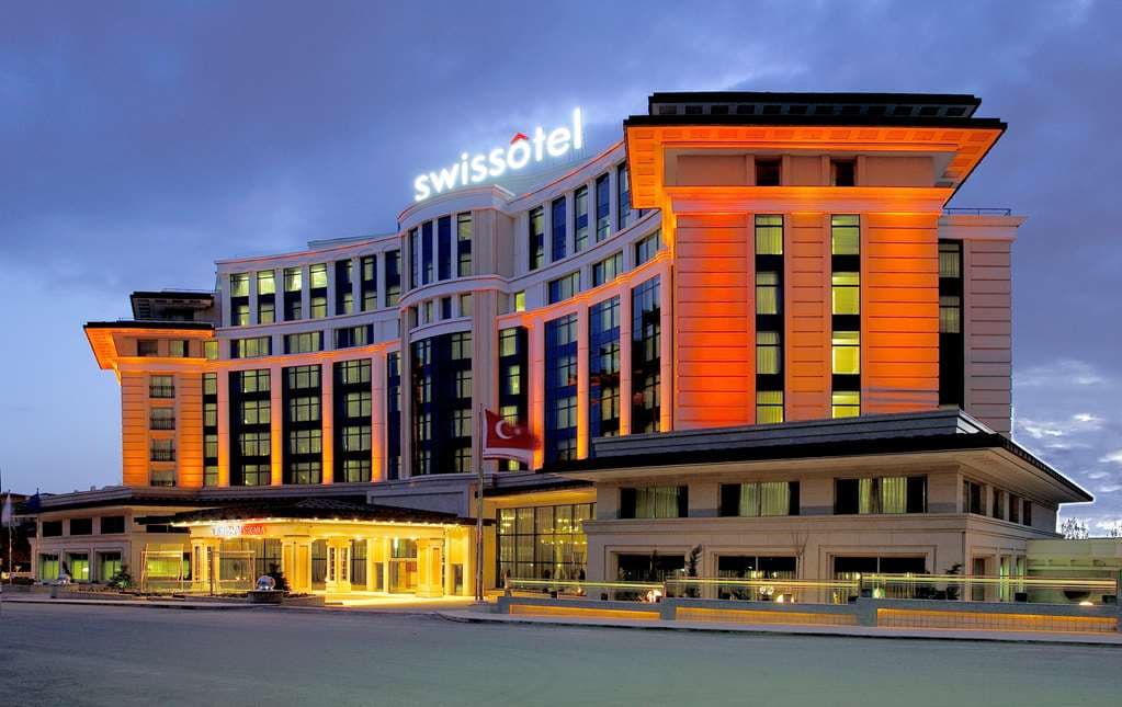 Symmetrical view of the Swissôtel Ankara half-olympic indoor pool with lounge chairs and soft lighting.