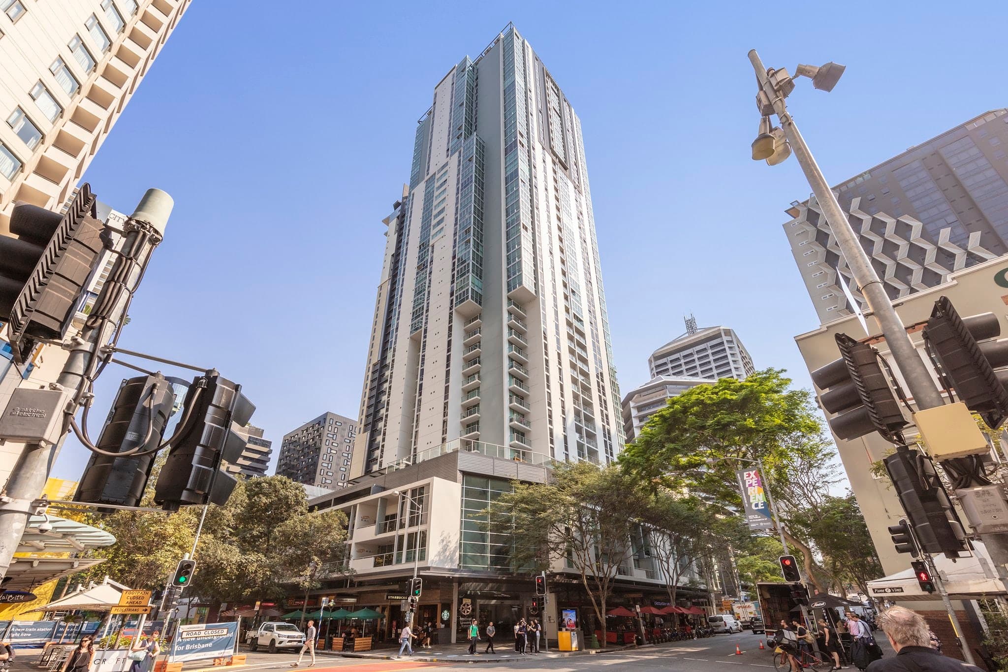 A sleek, heated 25-metre lap pool on a 4th-floor outdoor deck, framed by towering Brisbane CBD skyscrapers under a blue sky.