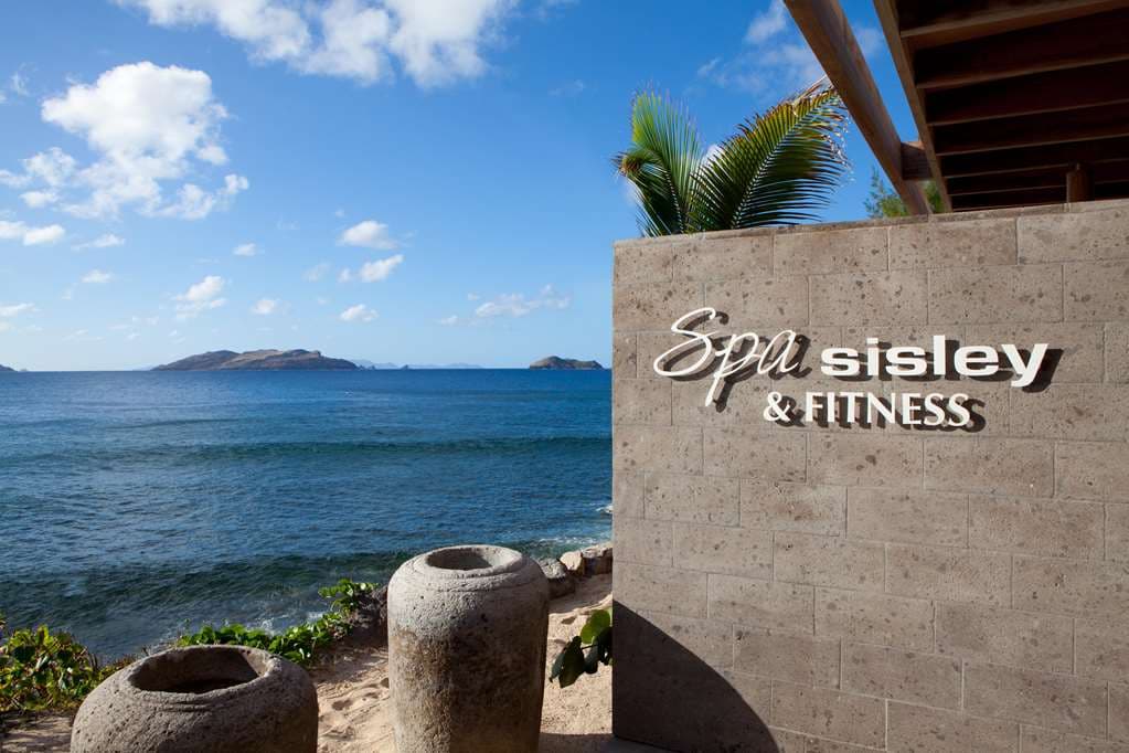 Curved infinity pool at Hotel Christopher Saint-Barth at sunset, with guests lounging under orange umbrellas and the ocean in the background.
