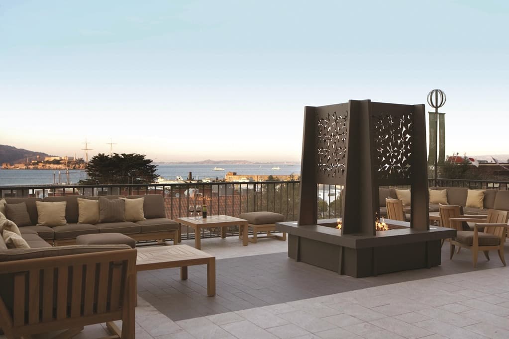 Guests relaxing by fire pits on the brick-lined Mustard Terrace at Fairmont Heritage Place, overlooking San Francisco Bay and Alcatraz.