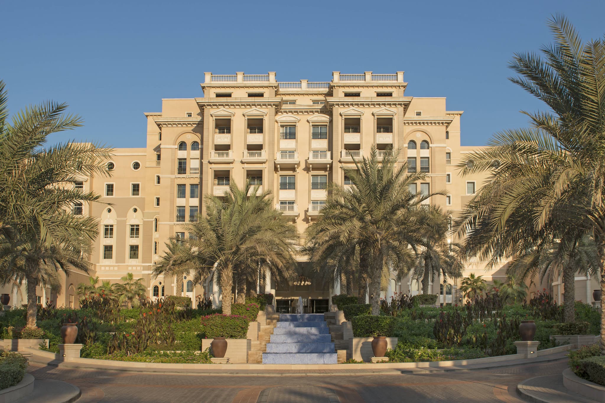 The neoclassical white facade of The Westin Dubai Mina Seyahi contrasted with the blue slides of Jungle Bay waterpark and lush palm gardens.