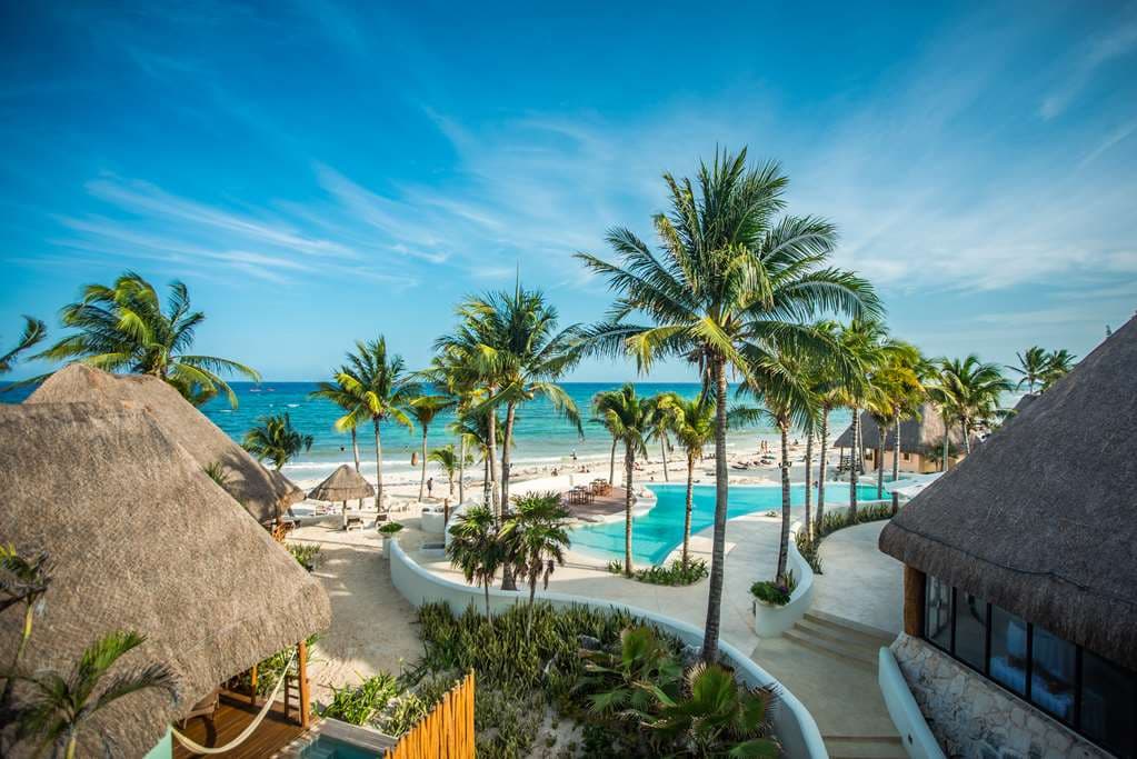 Mahekal Beach Resort infinity pool overlooking the Caribbean Sea with thatched-roof palapas and palm trees in the background.