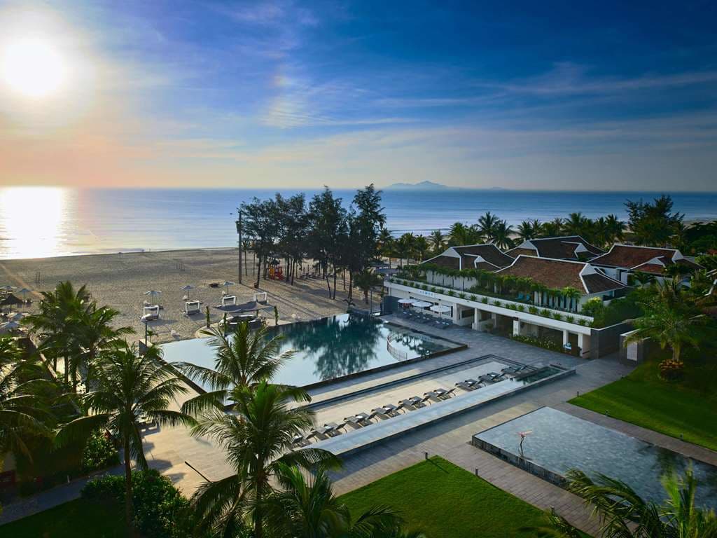 The illuminated 'Starry Sky' infinity pool at Pullman Danang at twilight, leading towards the private beach.
