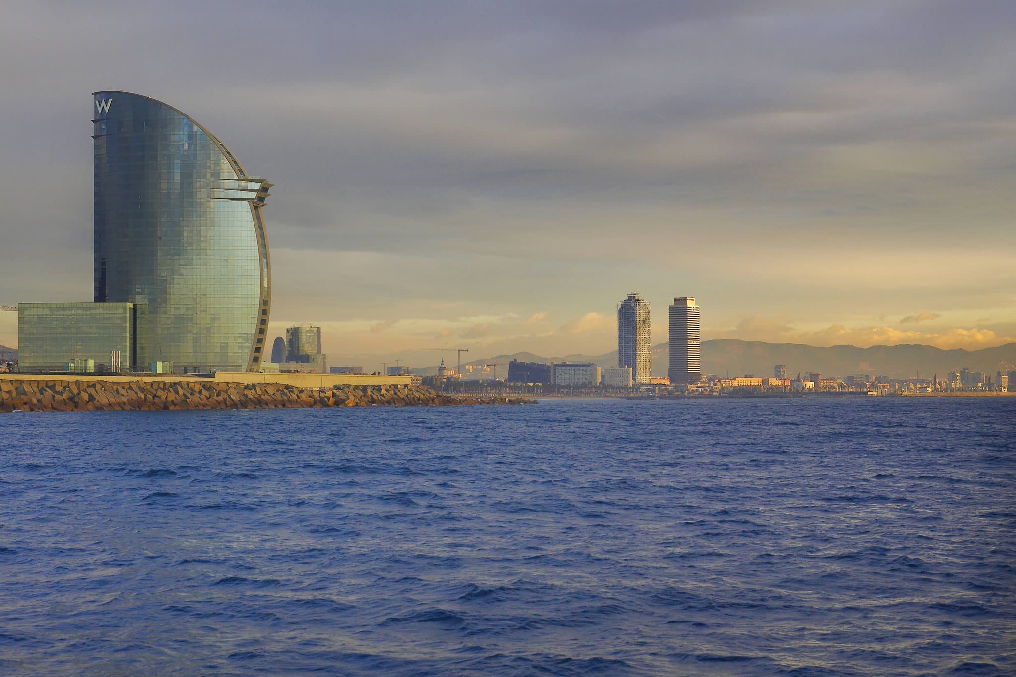 View of the sail-shaped W Hotel Barcelona rising above the Barceloneta boardwalk and Mediterranean Sea.