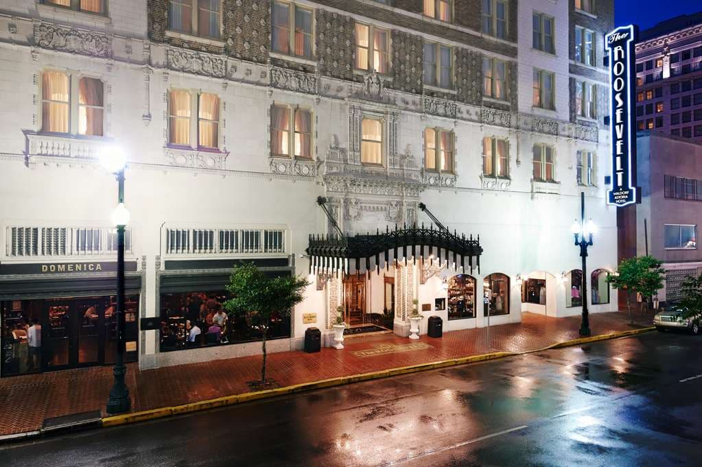 The dimly lit, block-long lobby of The Roosevelt New Orleans featuring crystal chandeliers and mosaic tile floors.