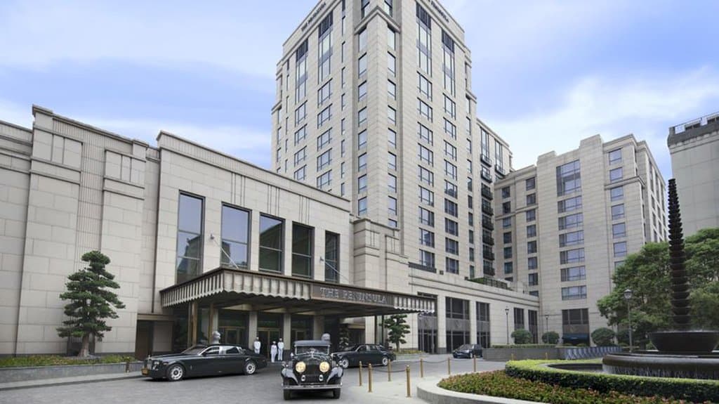 The Peninsula Shanghai exterior lit up at night with view of historic Bund architecture and vintage car in driveway