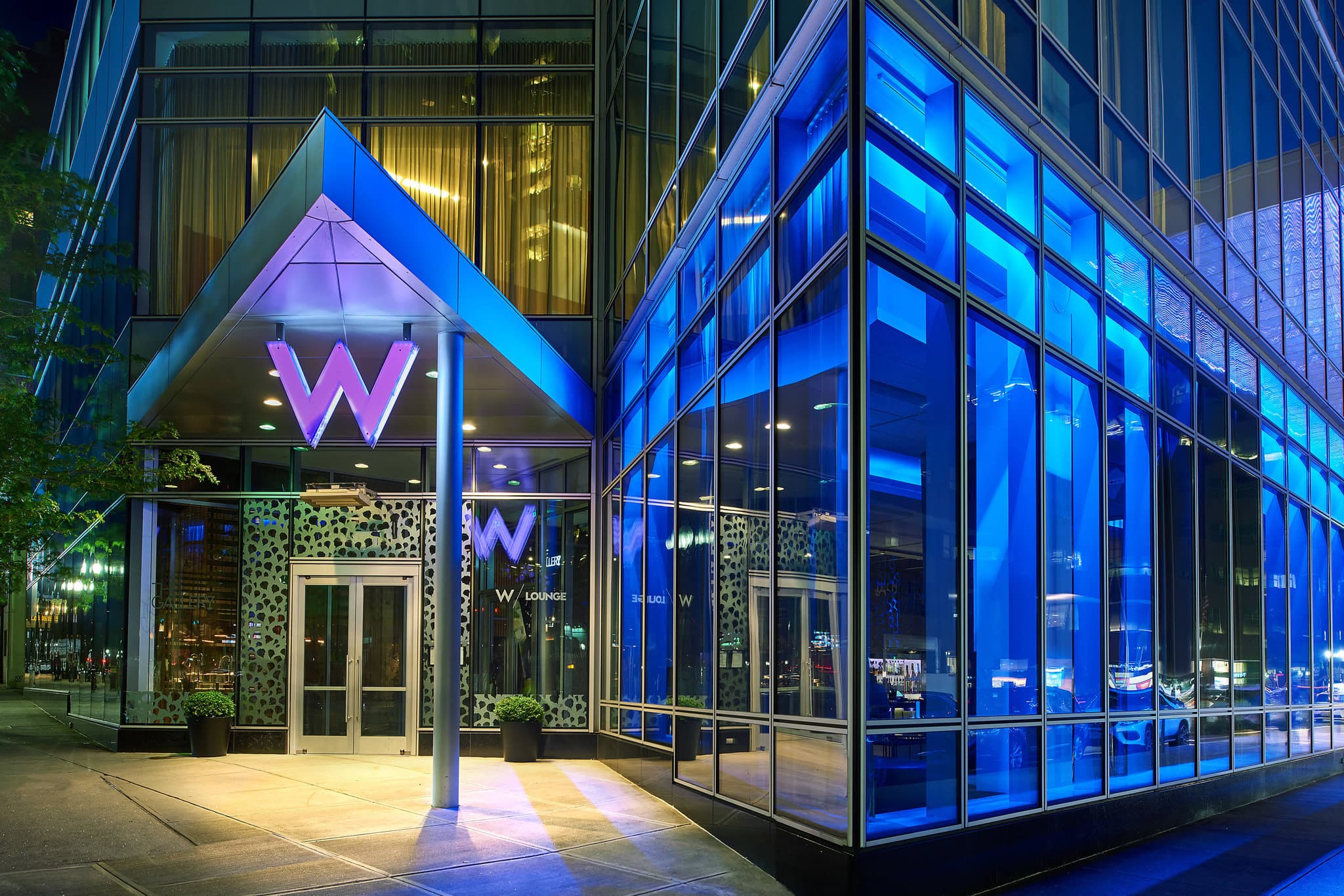 Low-angle shot of the W Boston glass façade at night with the digital marquee glowing red on Stuart Street.