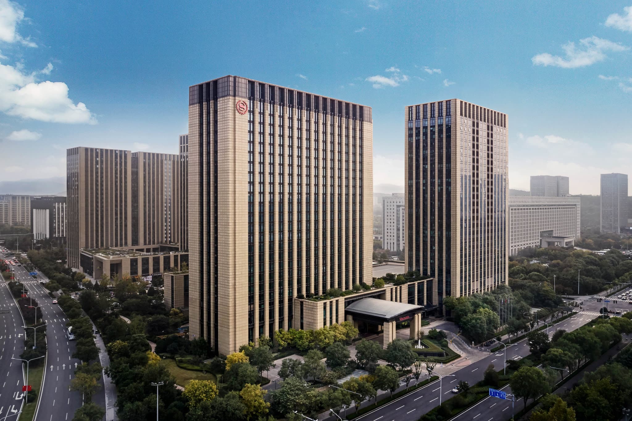 A low-angle night shot of the Sheraton Jinan Hotel exterior with the illuminated Jinan Olympic Sports Center in the background.