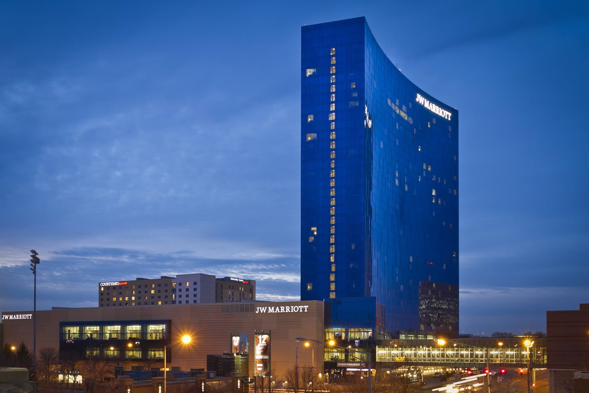 The curved blue glass façade of JW Marriott Indianapolis towering over the White River State Park green space.