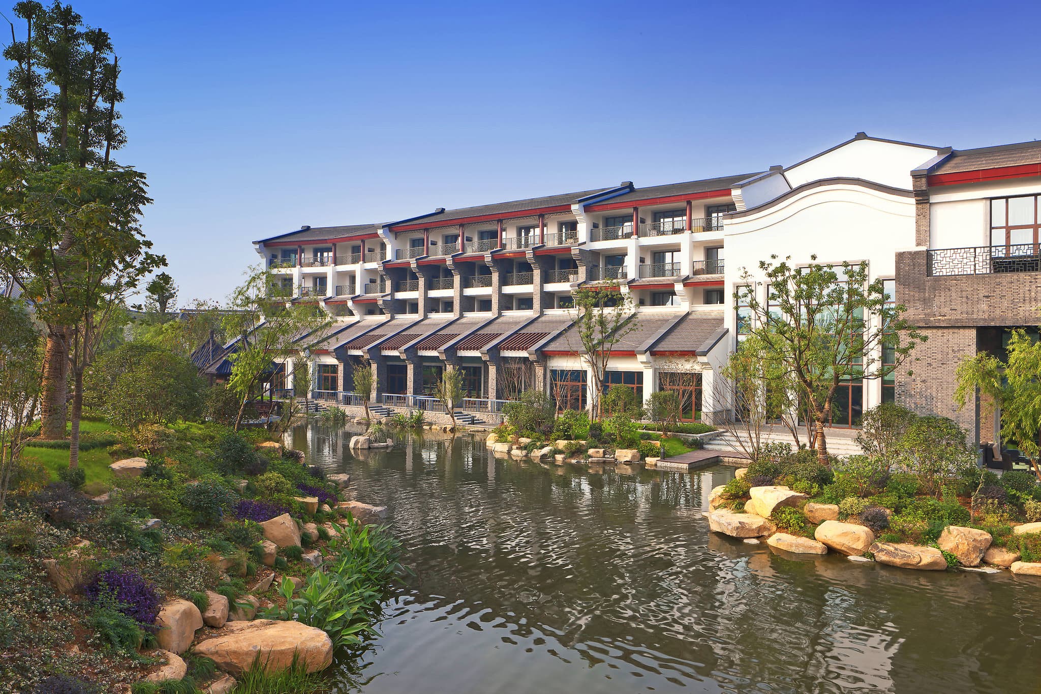 Traditional Jiangnan-style architecture of Sheraton Grand Hangzhou featuring dark tiled roofs and glowing lanterns reflected in a wetland pond.