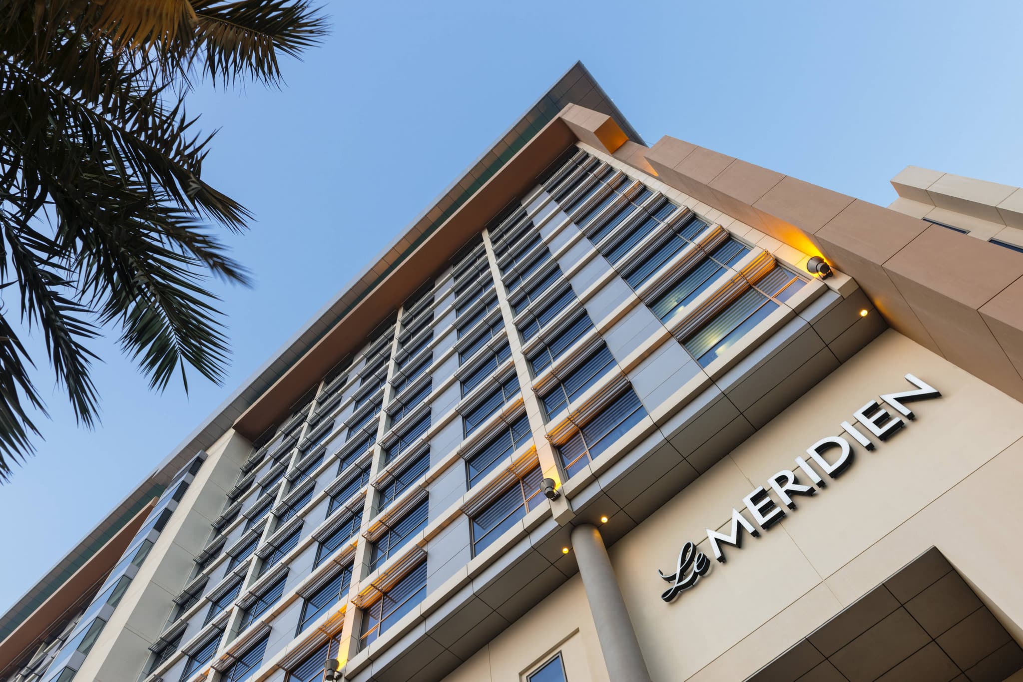 A sophisticated suite at Le Méridien Bahrain featuring neutral tones and art-deco lighting, overlooking the Manama skyline.