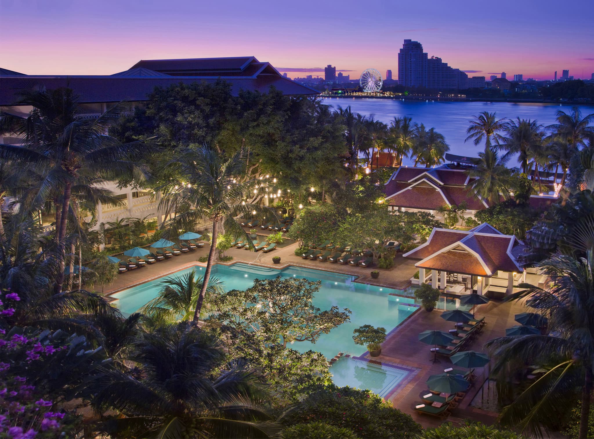 Anantara Riverside Bangkok Resort's massive lagoon pool surrounded by dense tropical palms and red umbrellas.
