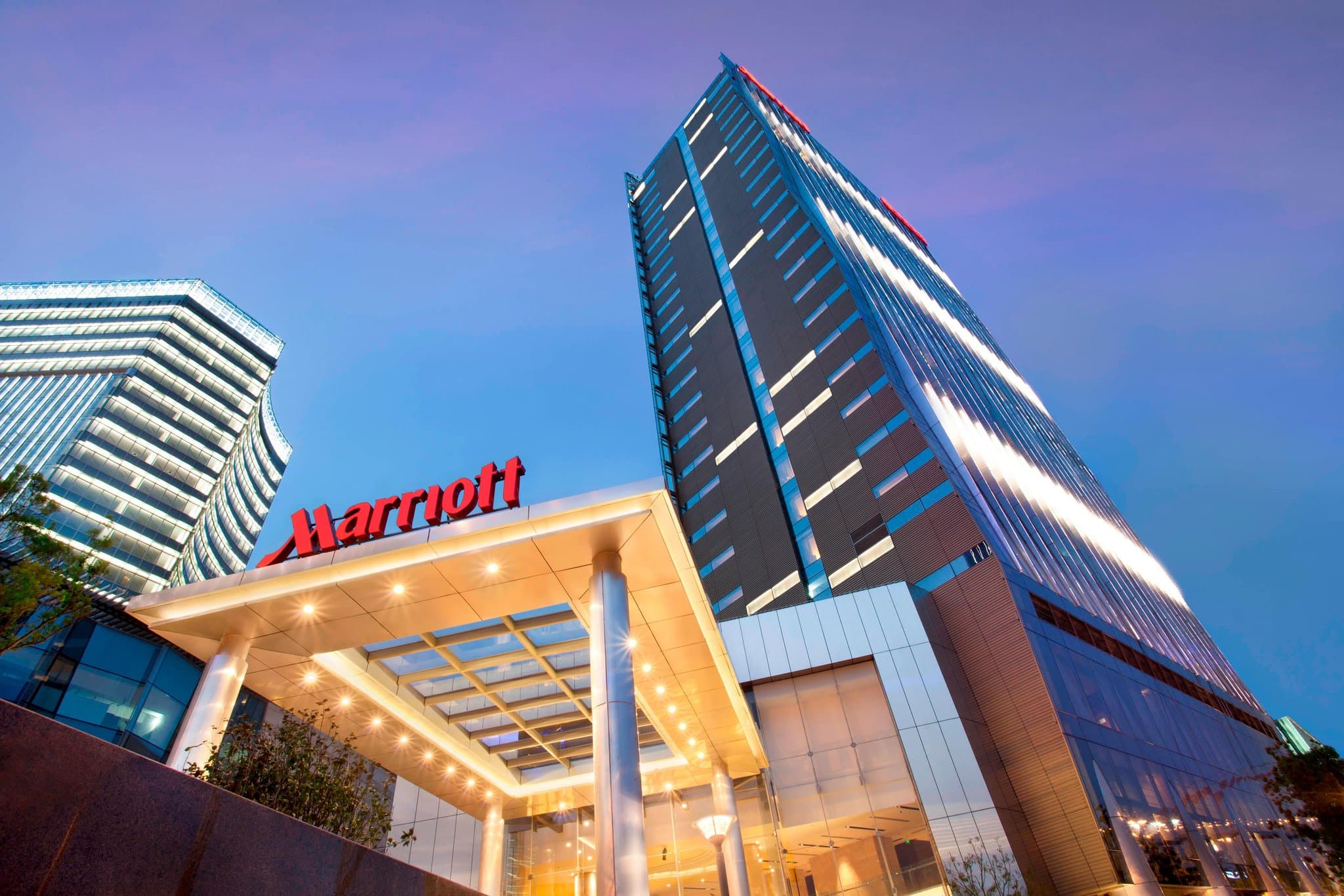 A dramatic dusk view of the Shanghai Marriott Hotel Riverside's glass façade reflecting the illuminated Lupu Bridge and Huangpu River.