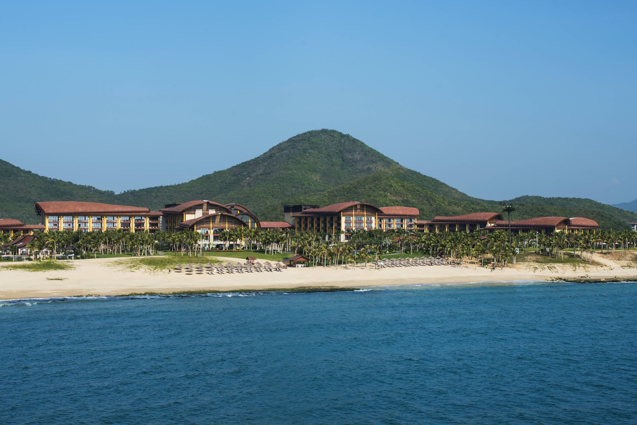 A serene infinity pool at The St. Regis Sanya Yalong Bay Resort overlooking a private marina and lush mangroves under a golden sunset.