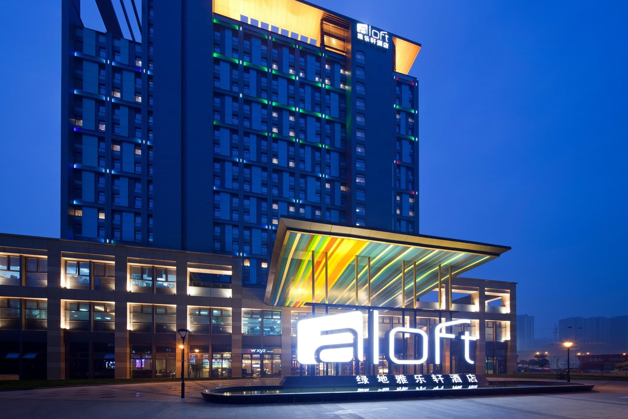 The W XYZ Bar at Aloft Zhengzhou featuring neon blue lighting, industrial exposed ceilings, and modern lounge seating.