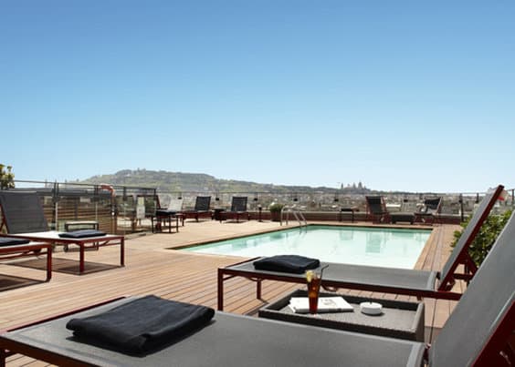 Hotel 1898 La Isabela rooftop terrace featuring striped sun loungers and a panoramic view of the Barcelona skyline.