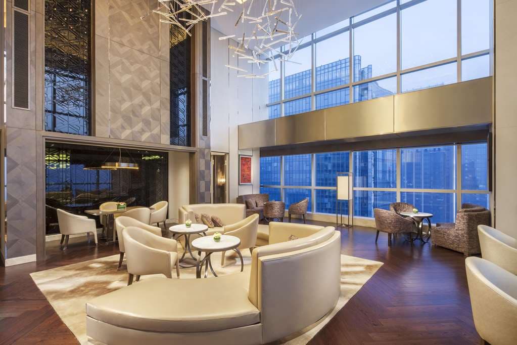 A serene, wood-paneled tea room at Hilton Chengdu featuring a traditional kungfu tea set against a backdrop of floor-to-ceiling city windows.
