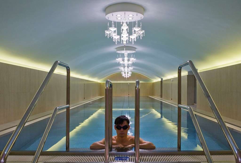 The 20-meter indoor lap pool at Hotel Sans Souci Wien, illuminated by multiple crystal chandeliers reflecting on the water.