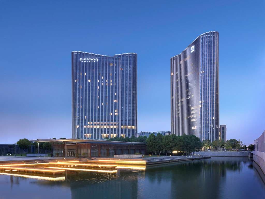 Low angle view of the Pullman Wuxi New Lake glass facade reflecting the blue sky, symbolizing modern corporate dominance.