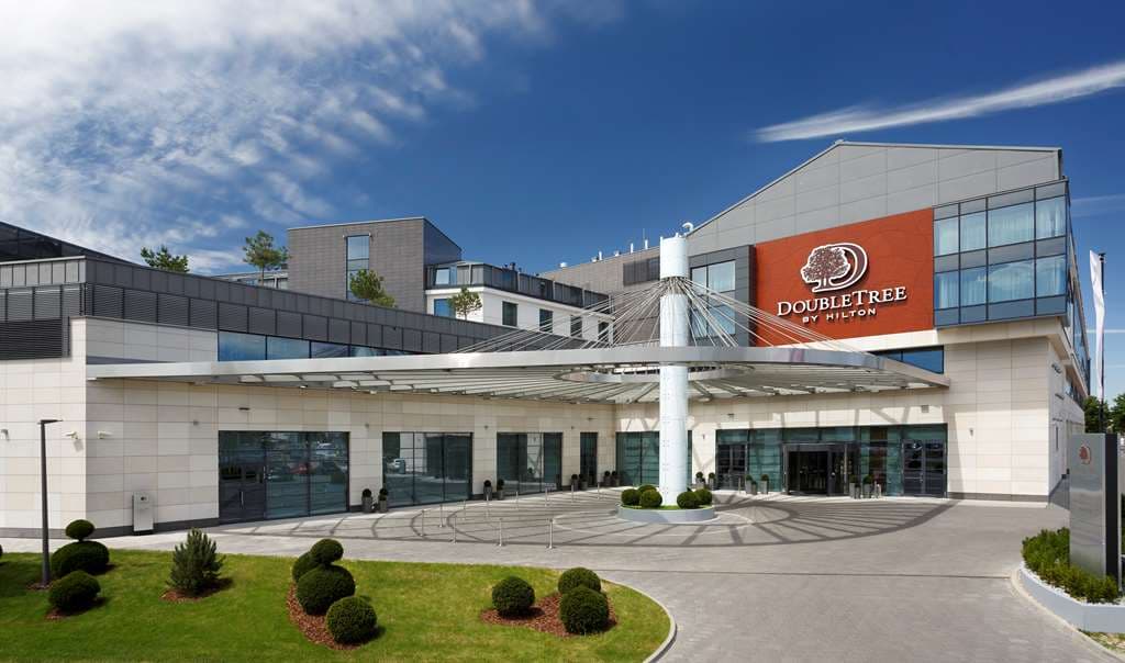 The curvaceous white facade of DoubleTree Warsaw reflecting beautifully in the outdoor garden pond during twilight.