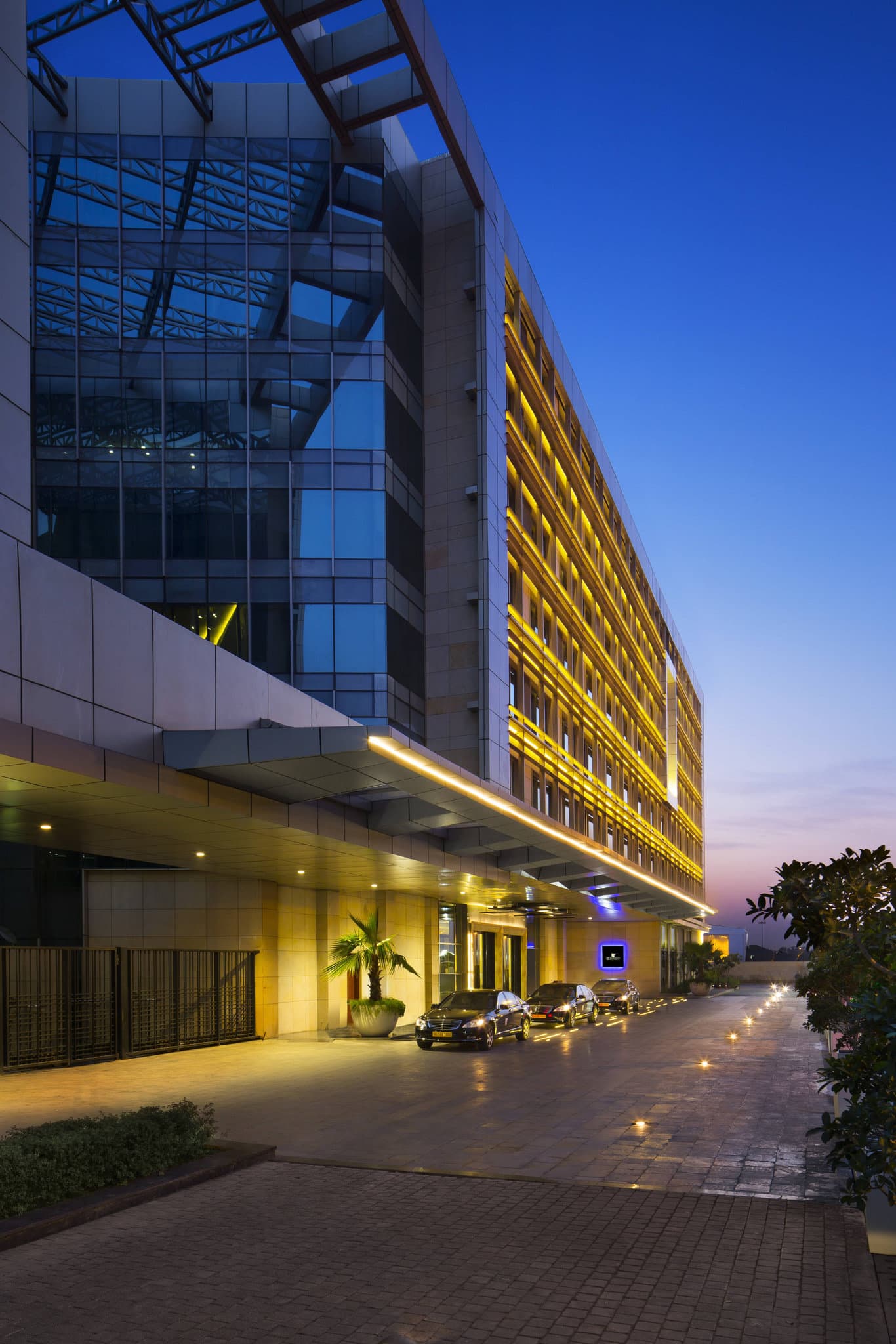 A sleek, modern hotel room at JW Marriott New Delhi with a large window overlooking the airport runway at dusk.