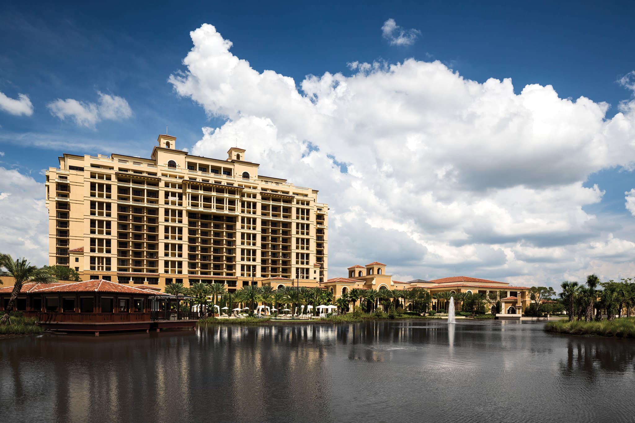 A twilight view of the Four Seasons Orlando's Spanish Revival facade lit by warm pool lights and palm trees.
