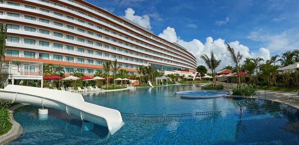 A high-angle view of the Hilton Okinawa Chatan Resort's lagoon pool with white curving architecture and blue water.