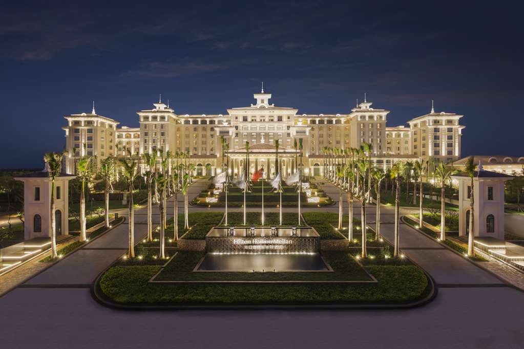 Twilight view of Hilton Haikou Meilan's castle-like exterior reflecting over the outdoor pool complex and Nandu River.