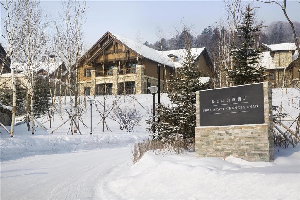夕暮れ時の長白山パークハイアット、雪に囲まれた屋外鉱泉プールから湯気が立ち上る様子。