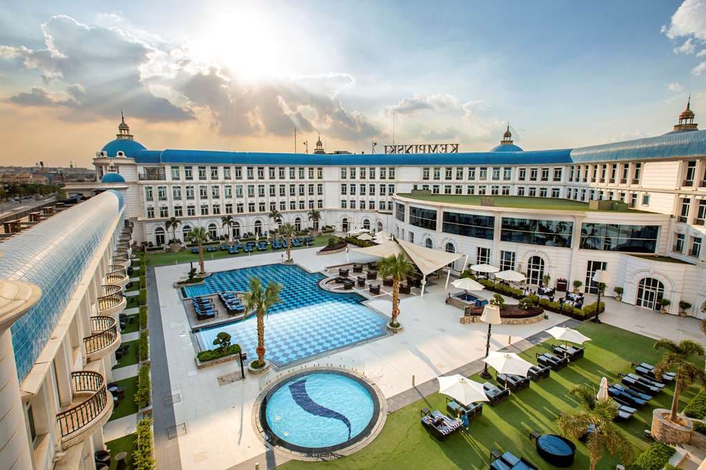 The central azure courtyard pool of Royal Maxim Palace Kempinski Cairo, framed by white palatial wings and blue domes.