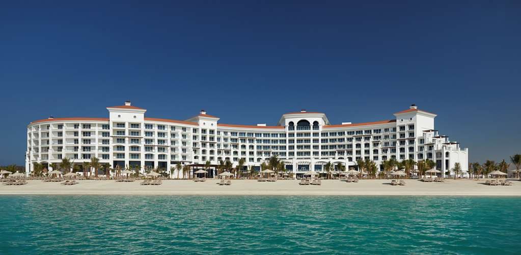 The symmetrical white marble facade of Waldorf Astoria Dubai Palm Jumeirah reflecting in the main pool at twilight.