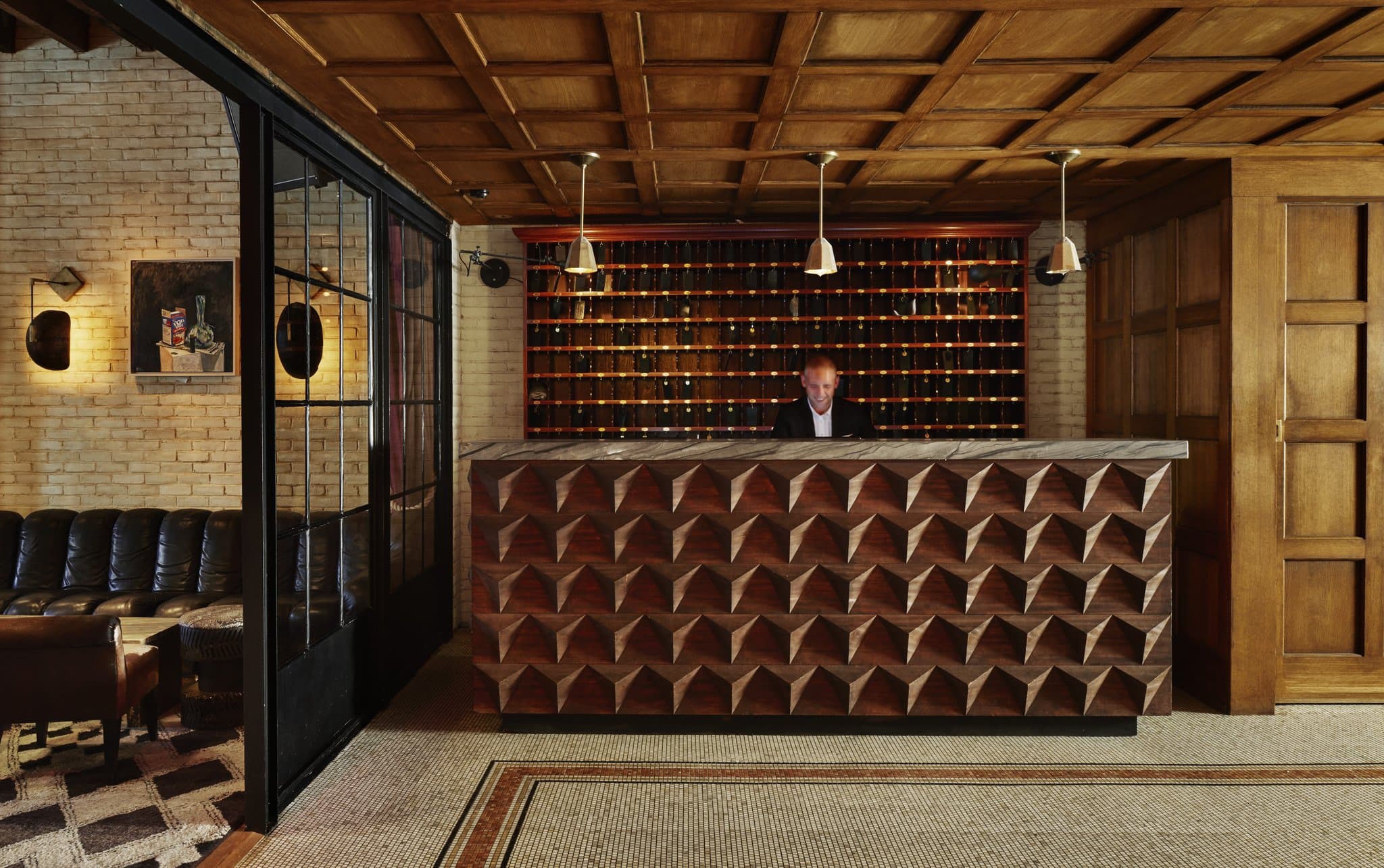 The Ludlow Hotel lobby featuring a limestone fireplace, velvet armchairs, and factory-style windows.