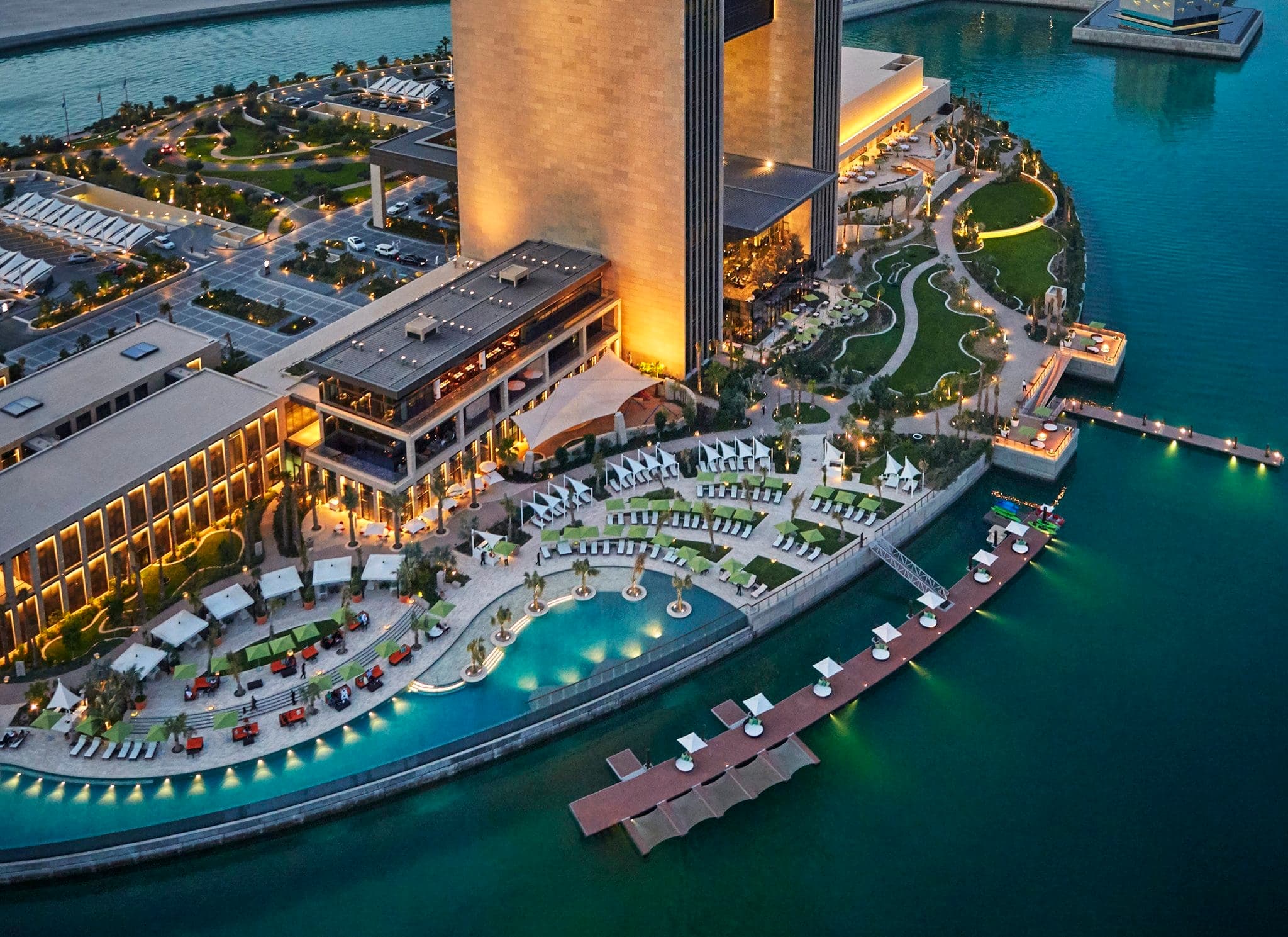 The H-shaped exterior of Four Seasons Bahrain Bay illuminated at night, reflecting off the water.