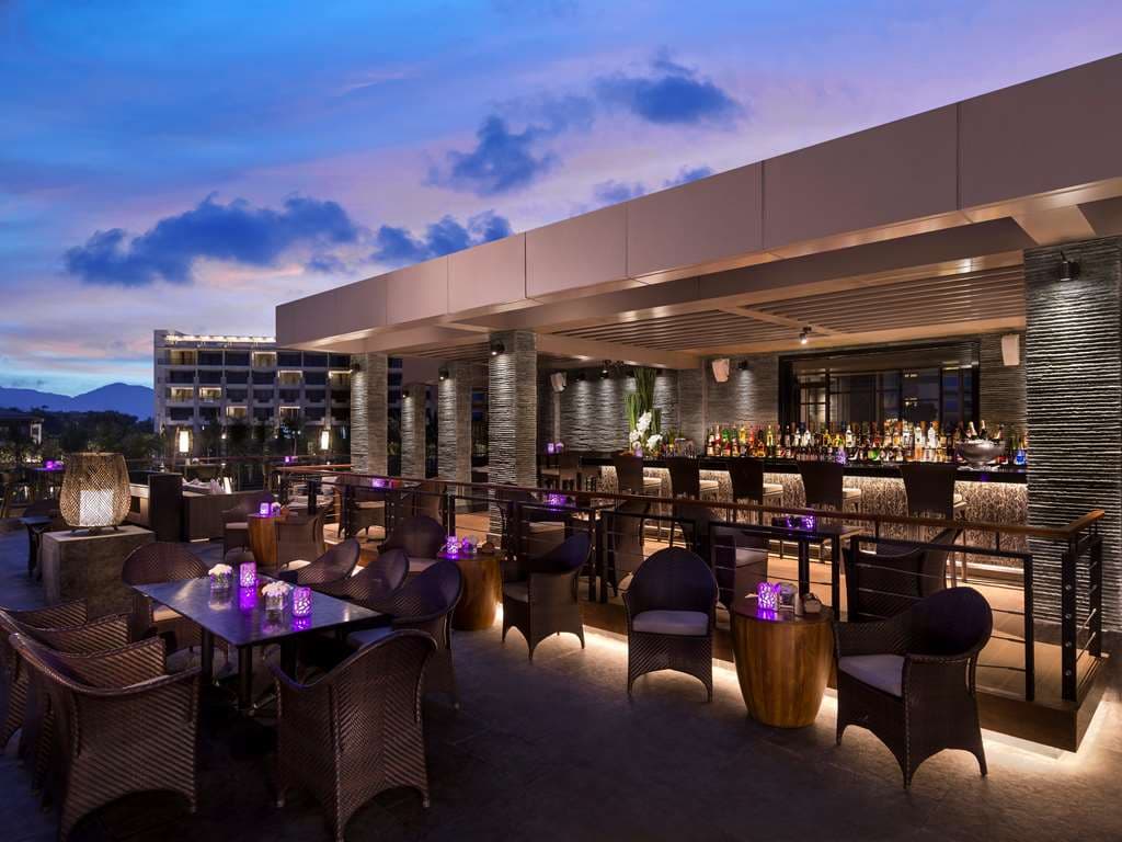 A dramatic dusk view of the Shangri-La Sanya's open-air Kon Tiki restaurant with thatched roofing and tiki torches illuminating the tropical landscaping.
