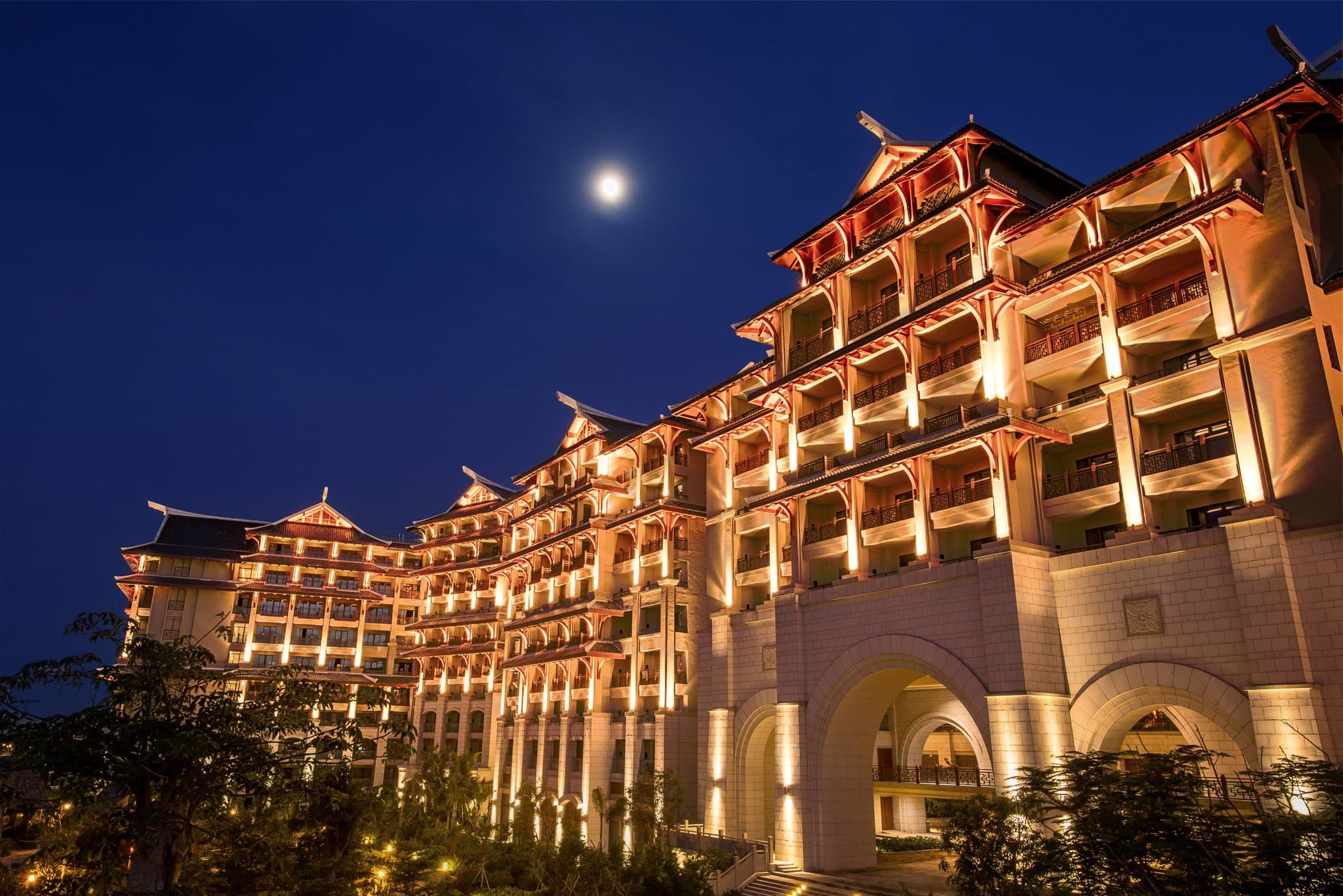 The Haikou Marriott Hotel's central outdoor pool complex at twilight, framed by illuminated pagoda-style towers and palm trees.