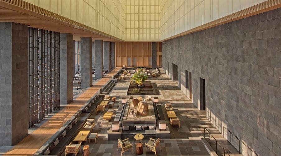 A dramatic shot of Aman Tokyo's lobby featuring the soaring 30-meter washi paper lantern ceiling and a central seasonal ikebana arrangement.