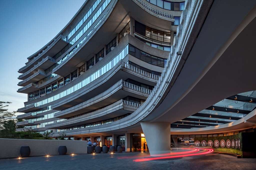 The Watergate Hotel's rooftop bar, Top of the Gate, at twilight with the Washington Monument glowing in the distance and guests holding cocktails.