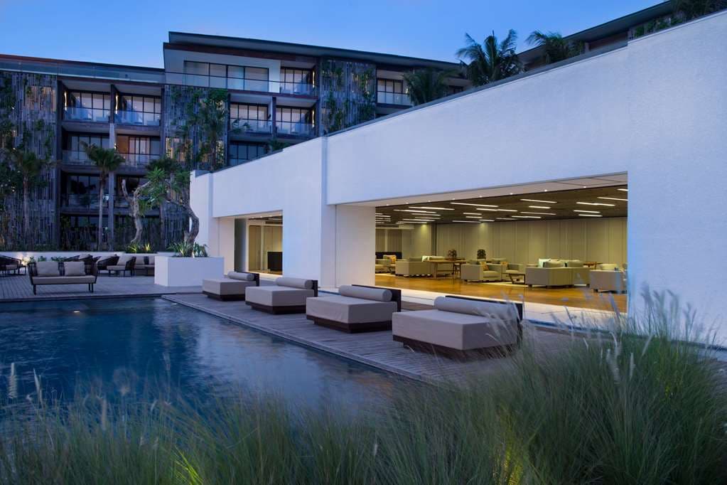 Infinity pool at Alila Seminyak reflecting the sunset, framed by vertical gardens and modern concrete architecture.