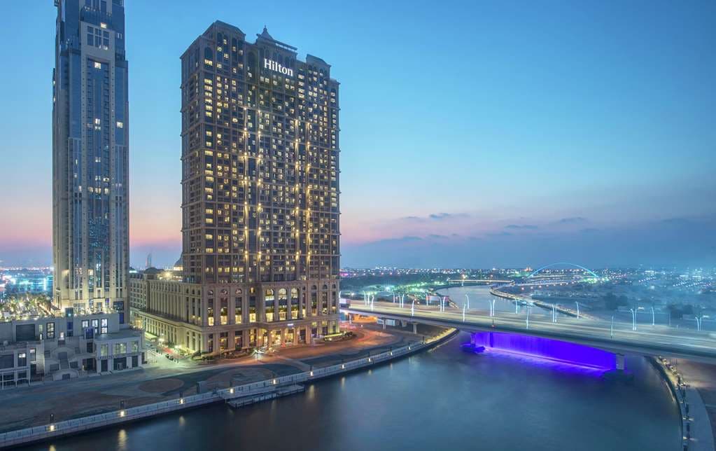 View from Hilton Dubai Al Habtoor City showing the illuminated Dubai Water Canal and the Burj Khalifa skyline at dusk.