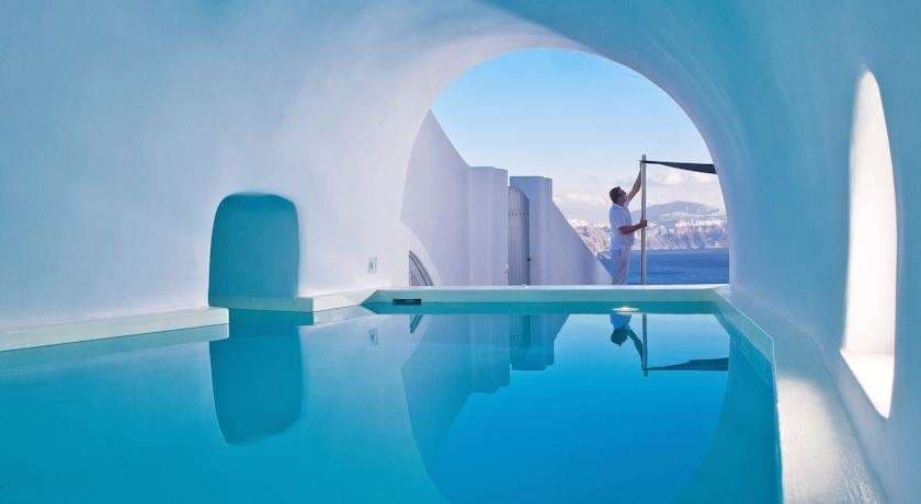 A dramatic view of Andronis Luxury Suites' infinity pool perched on the Oia cliffs, overlooking the volcanic caldera at sunset.