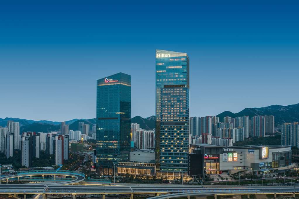 A dramatic silhouette of a swimmer in the heated indoor pool on the 33rd floor, framed by floor-to-ceiling windows overlooking the Jinan skyline.