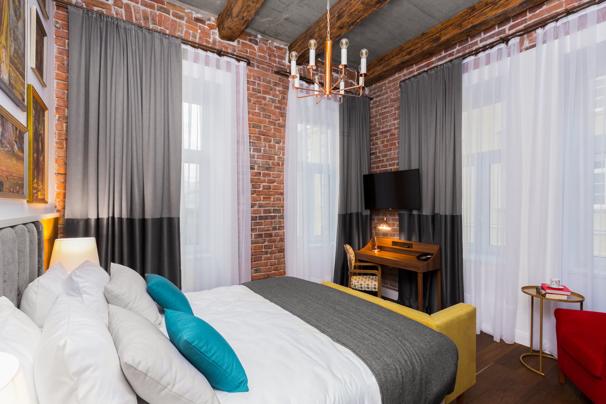 A moody, art-filled hotel room at Hotel Indigo Krakow featuring a teal velvet armchair, dark walls, and a wardrobe open to reveal a vibrant jungle print interior.